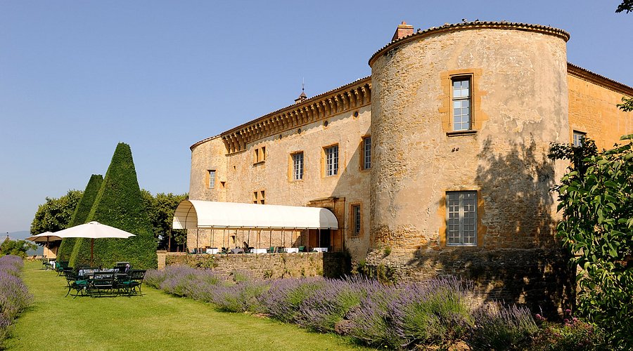 A stone house with a round tower and a row of lavender along the wall.
