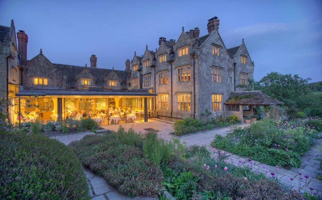 A stone manor at dusk, with a lit glass dining room opening onto the garden.