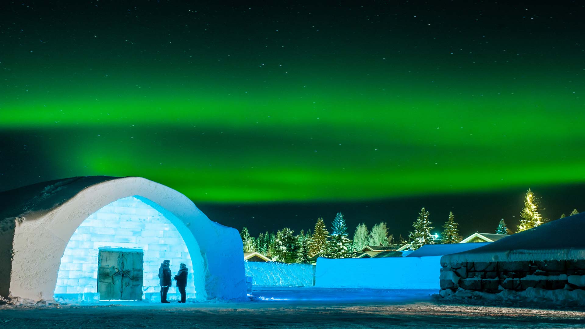 An ice building lit from within under a green night sky.