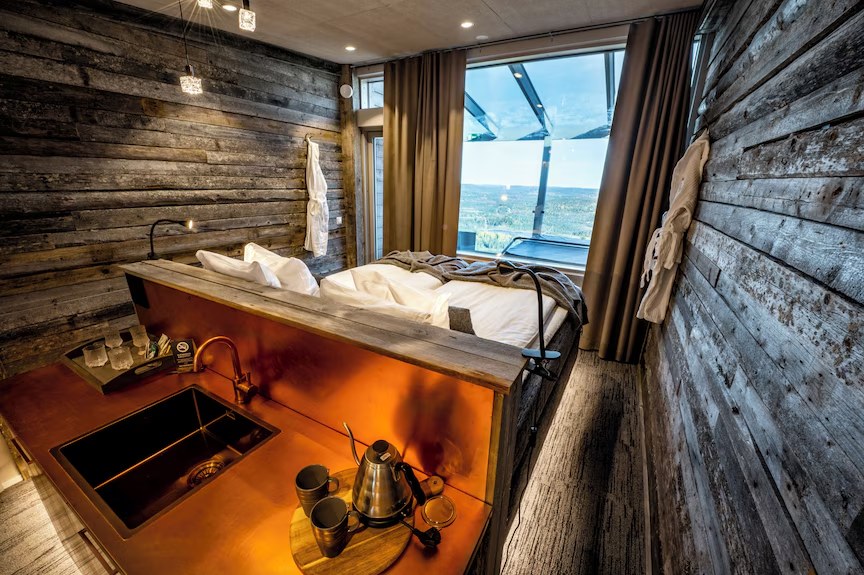 A wooden cabin room with a copper kitchen counter and a wide view of forested hills.